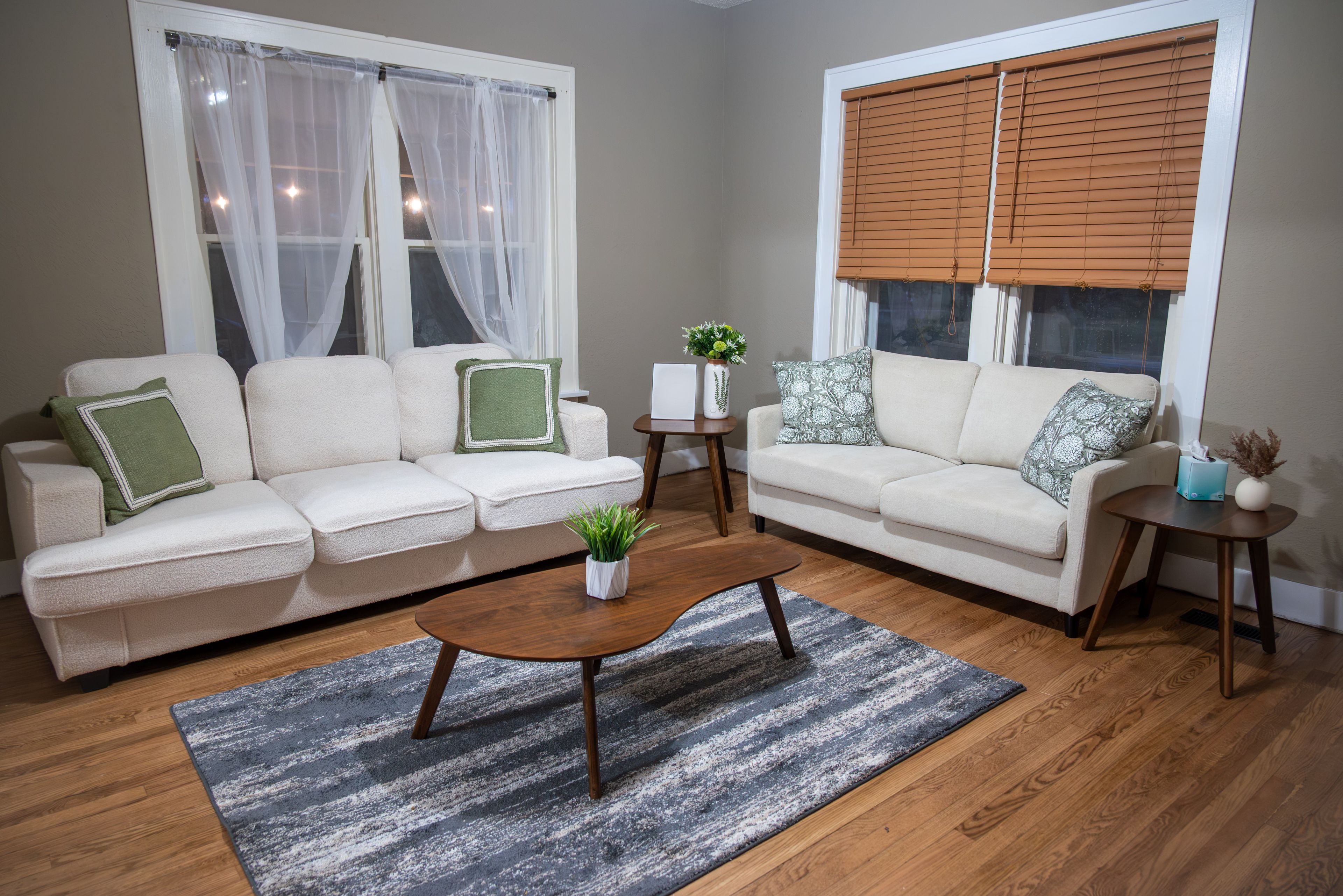A living room with two sofas, a coffee table, a small side table, and a window with blinds.