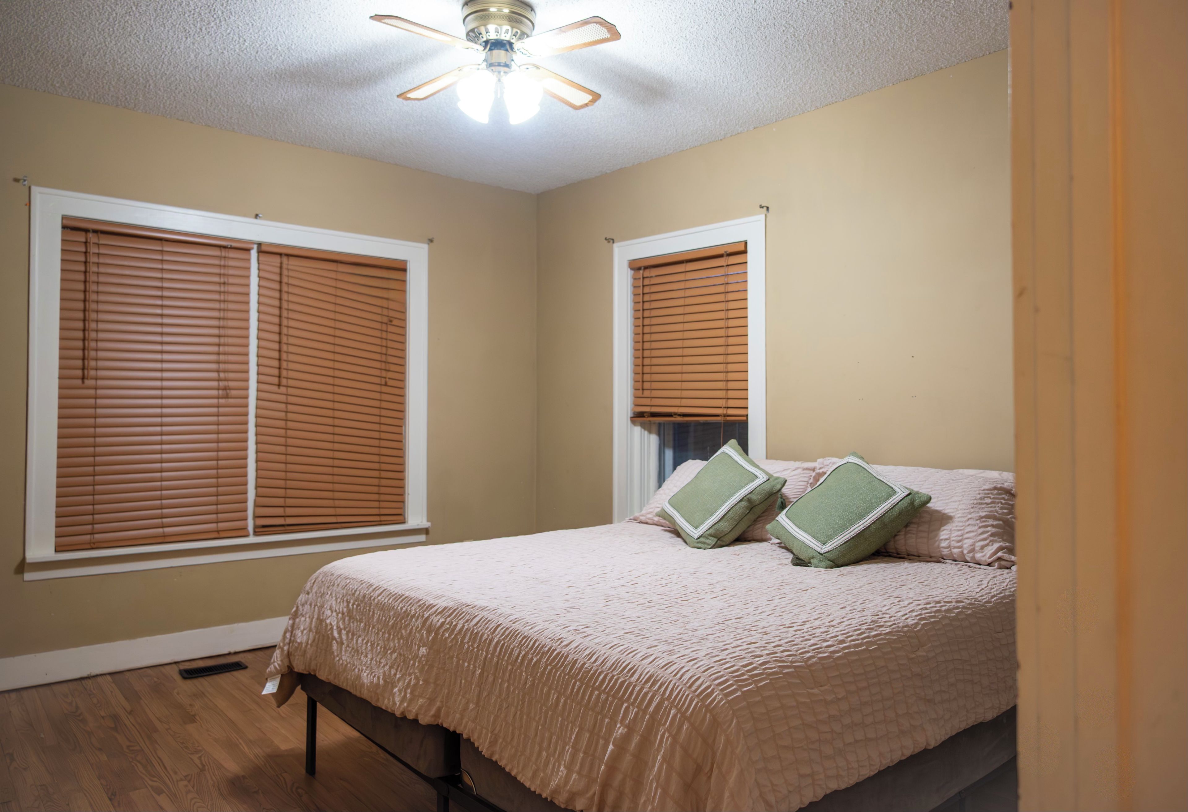Une chambre avec deux fenêtres, un lit recouvert d’une courtepointe et un ventilateur de plafond.