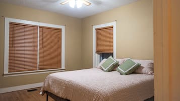 Une chambre avec deux fenêtres, un lit recouvert d’une courtepointe et un ventilateur de plafond.