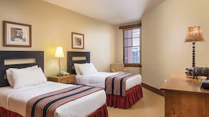 Una habitación de hotel con dos camas, una mesita de noche con lámpara, una silla y un escritorio con lámpara.