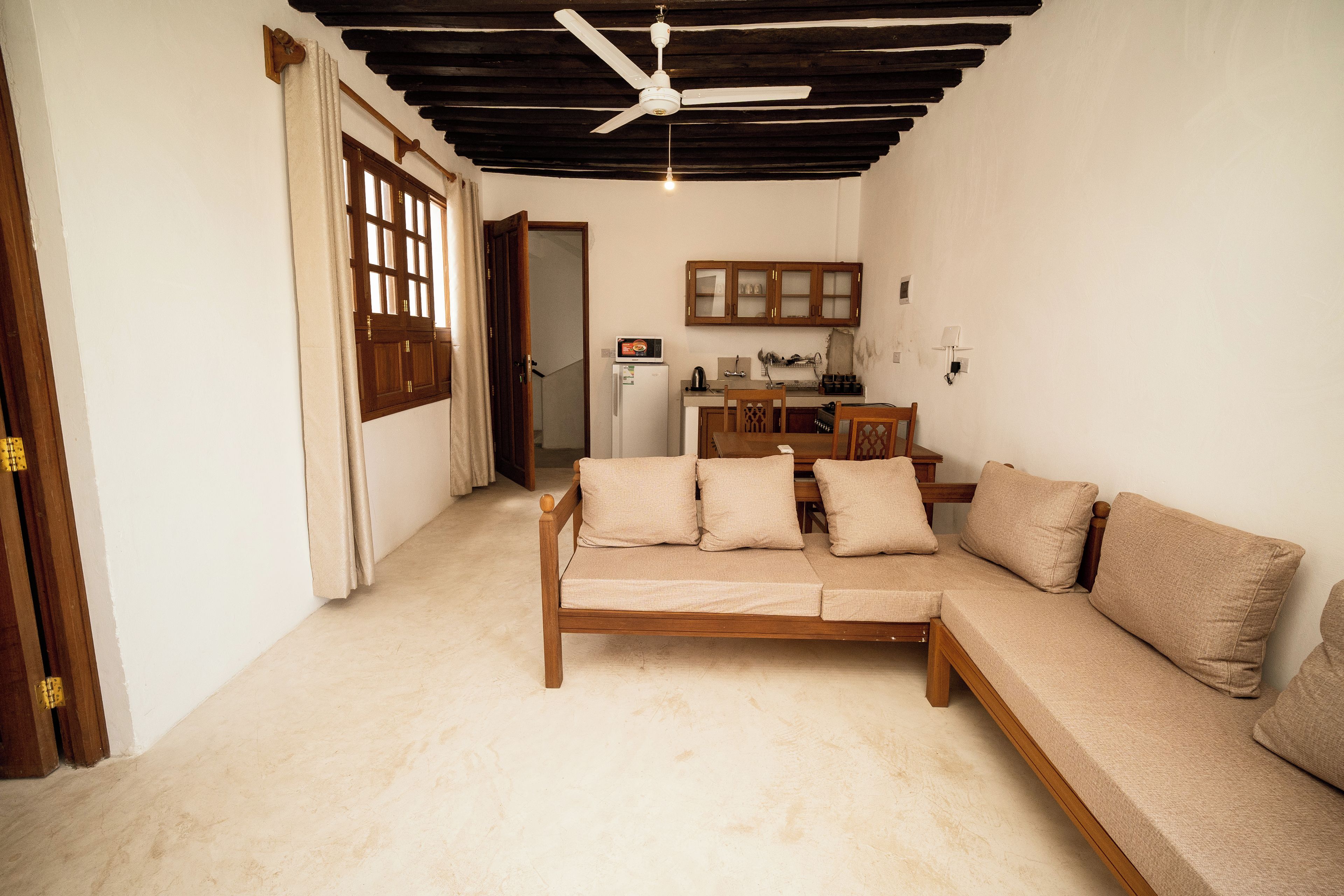 Sala de estar com sofá, ventilador de teto e cozinha com armários e geladeira.
