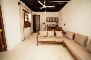 A living room with a sofa, a ceiling fan, and a kitchen area with cabinets and a refrigerator.
