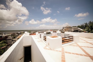 A rooftop terrace with white walls and terracotta tiles, overlooking a body of water and a distant shoreline.