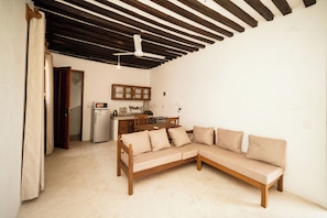 A room with a wooden sofa, a kitchen area, and a dining table.