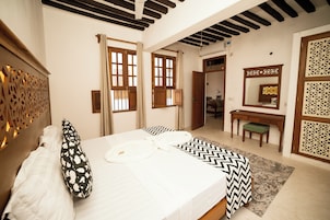 Un dormitorio con una cama, un escritorio, un espejo y una puerta que da a otra habitación.
