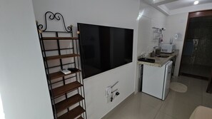 A compact living space with a flat-screen TV mounted on the wall, a small kitchenette with a microwave, and a compact refrigerator. - MicroEstudio Intermares - 100m from the sea + cost-benefit (Cabedelo)