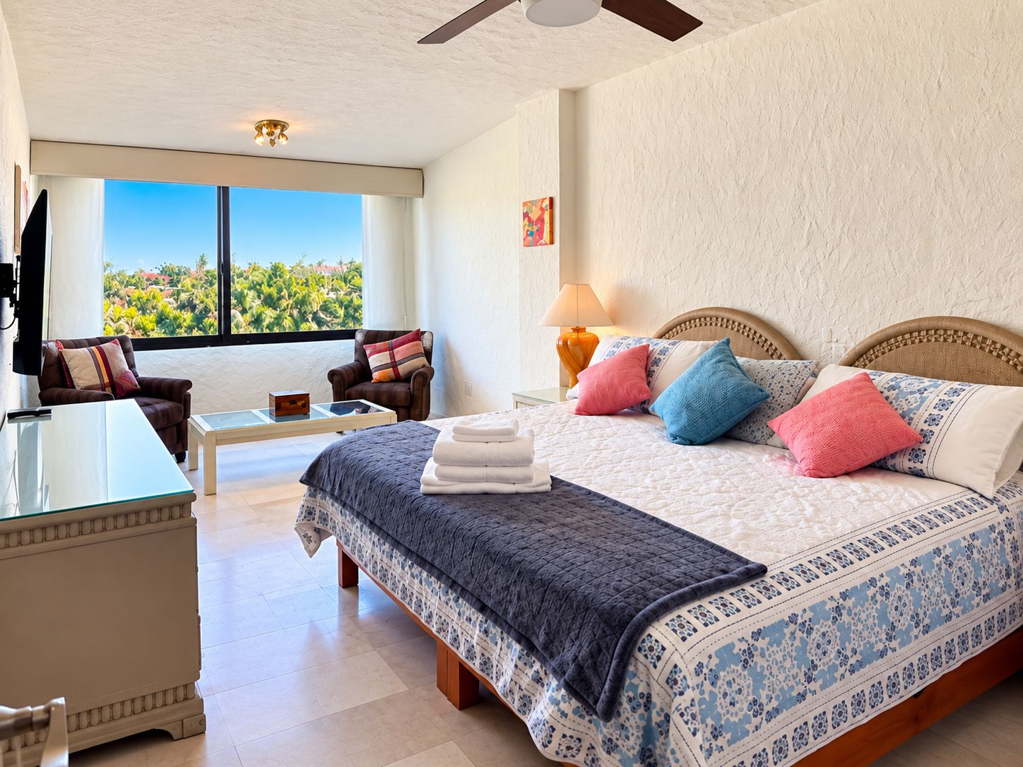 Ein Hotelzimmer mit einem großen Bett, einem Schreibtisch, einem Stuhl, Blick ins Freie und einem Deckenventilator.