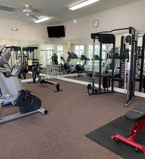Ein Fitnessstudio mit unterschiedlichen Trainingsgeräten, darunter Laufbänder, ein Kraftgerät und eine Spiegelwand.