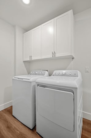 A laundry room with two white washing machines and a white cabinet above them. - Cherry Cove | Beach Access | AC | BBQ | Dbl Garage (Invermere)