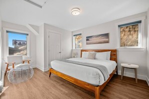 A bedroom with a wooden bed, a chair, a small table, and a window with a view. - Cherry Cove | Beach Access | AC | BBQ | Dbl Garage (Invermere)