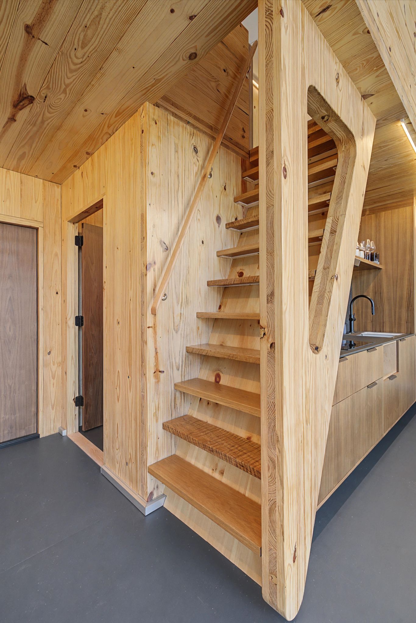 Un escalier en bois avec un coin cuisine en bas, comprenant un évier et des placards.