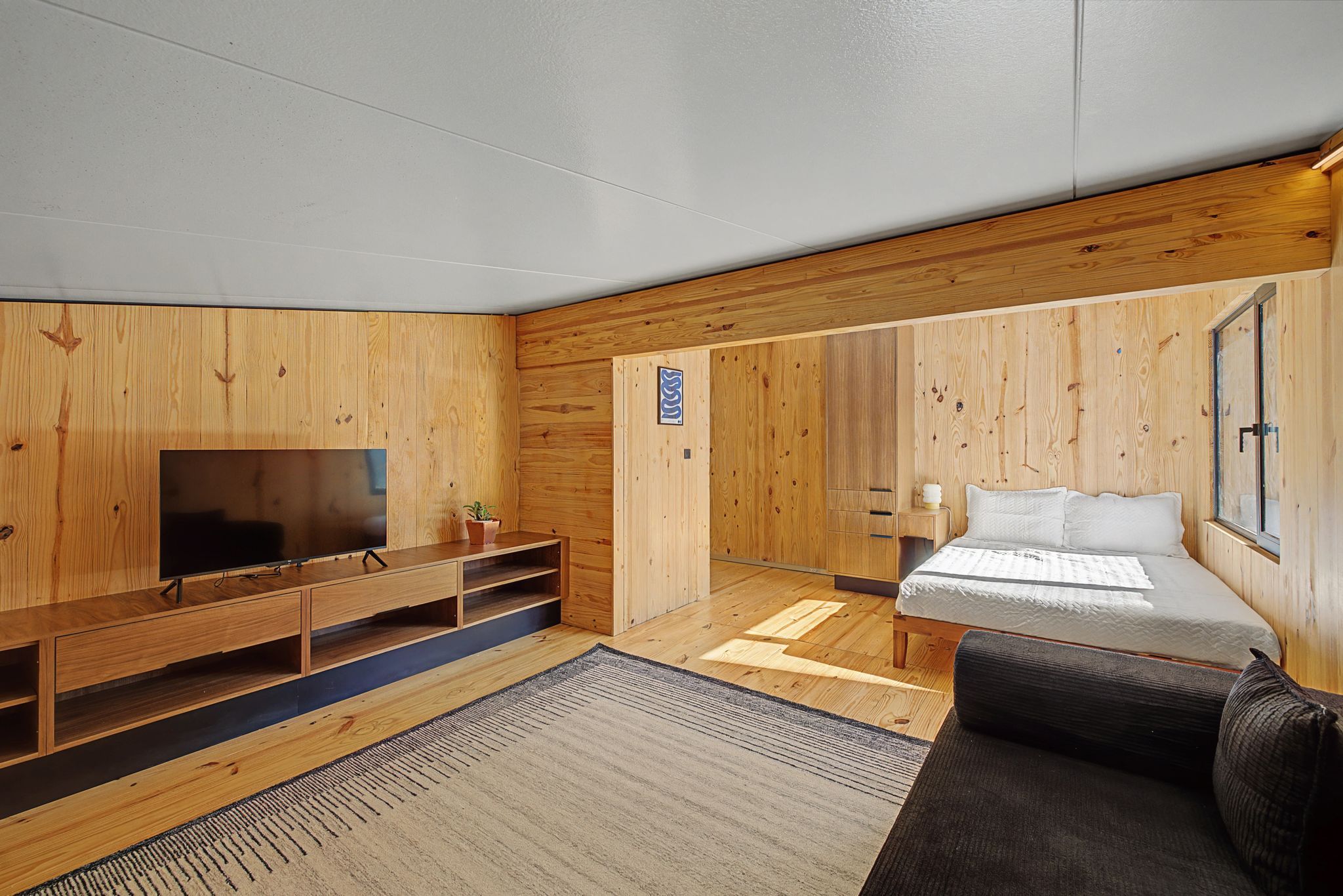 Een kamer met een houten wandpaneel, een bed, een televisie, een bank en een klein tafeltje.
