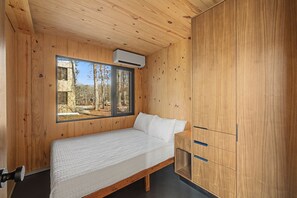 Ein Zimmer mit Holzwänden, einem Bett, einem Fenster und einem Einbauschrank.