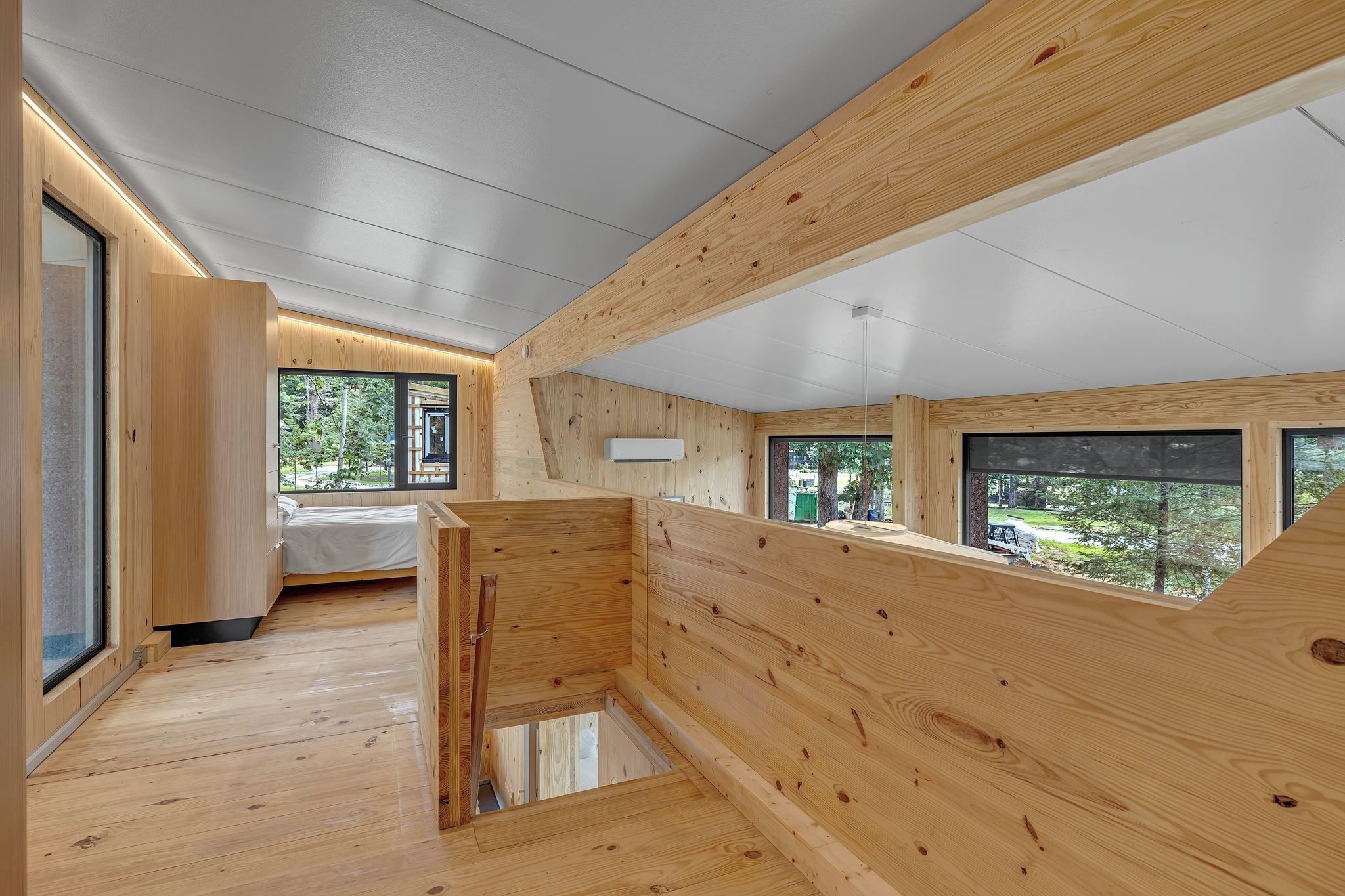 Un intérieur moderne avec des poutres en bois, un lit et de grandes fenêtres offrant une vue sur l’extérieur.