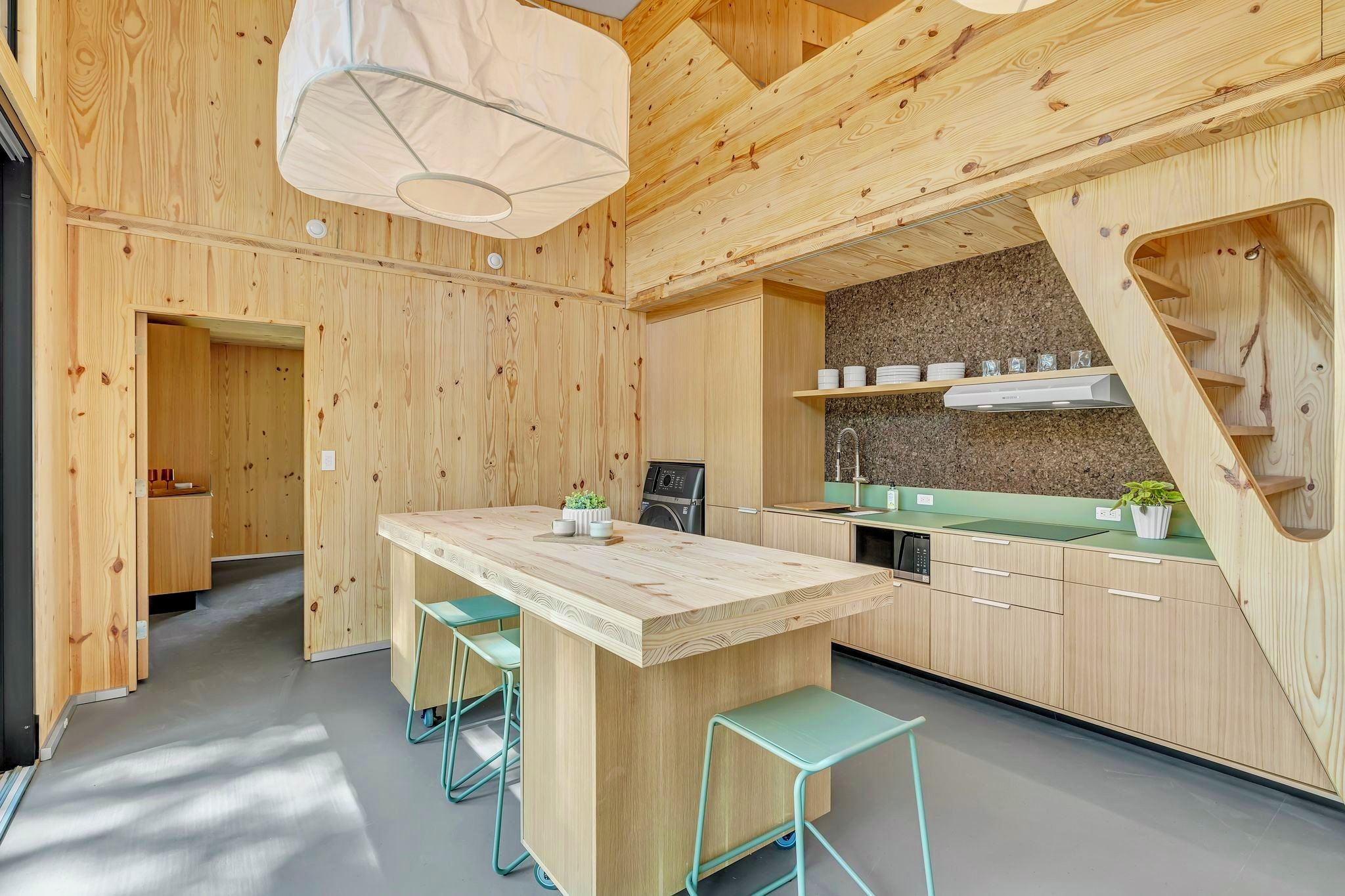 Eine moderne Küche mit Holzschränken, einer zentralen Kochinsel, Barhocker, einem eingebauten Backofen und einer Spüle aus Edelstahl.