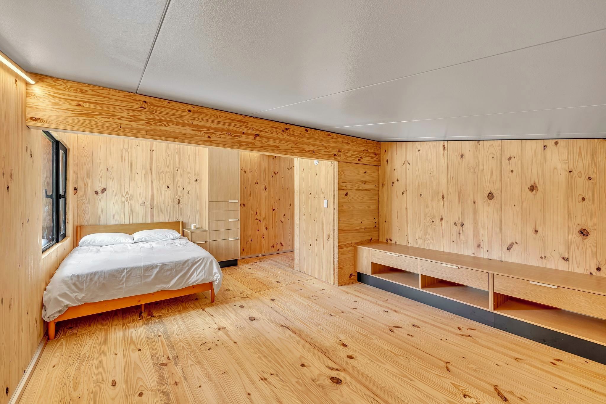 Ein Schlafzimmer mit Holzboden, einem Bett, einer Bank und eingebauten Schränken.