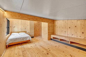 Ein Schlafzimmer mit Holzboden, einem Bett, einer Bank und eingebauten Schränken.
