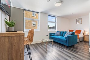 A modern living room with a blue sofa, a glass coffee table, and a wicker chair. - Sutherland Apartments - Apt 27 (London)