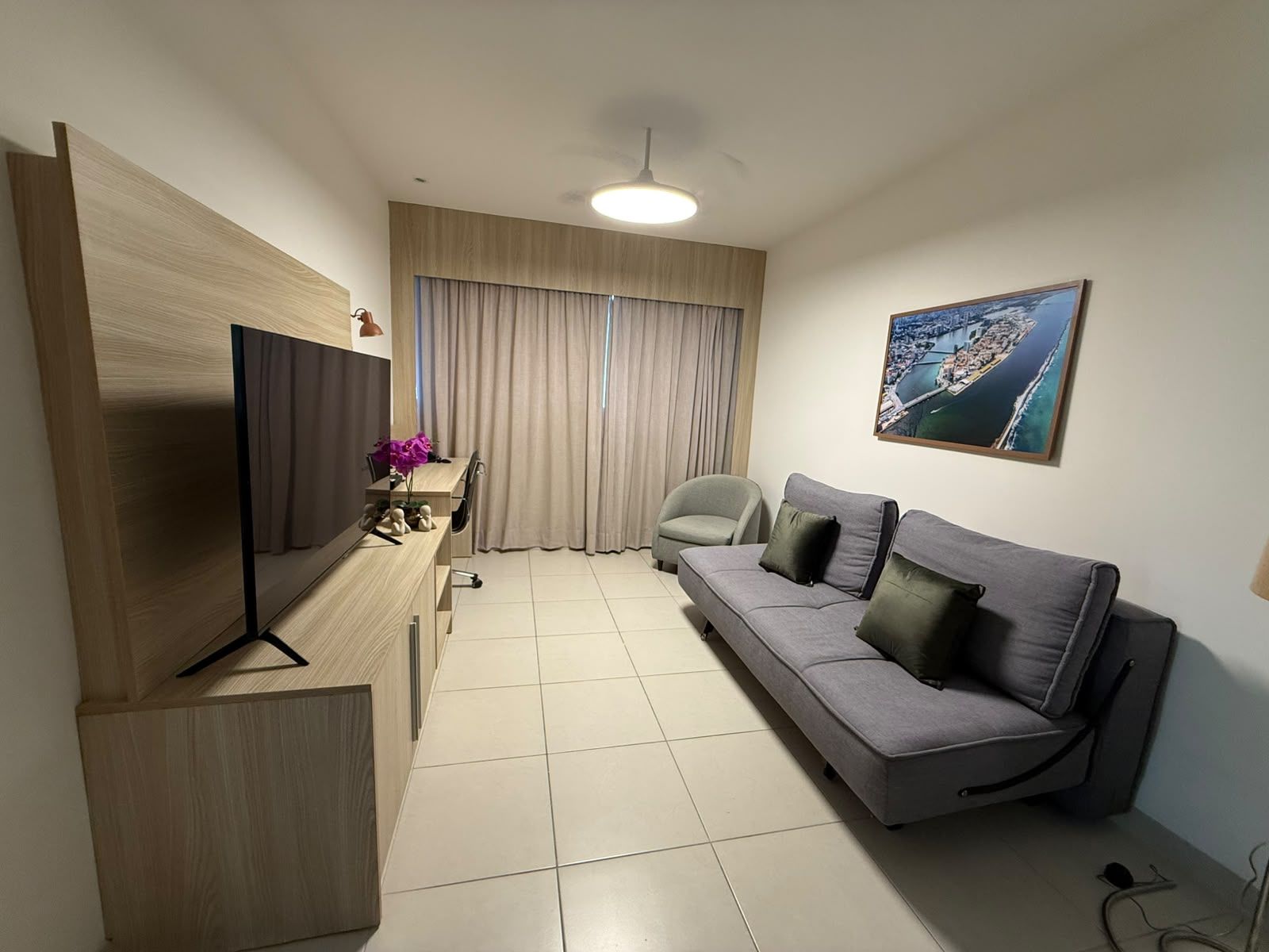 A modern living room with a flat-screen TV, a sofa, a chair, and a painting on the wall.