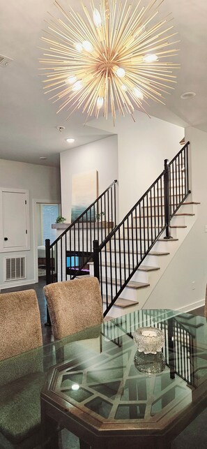 A modern interior with a glass coffee table, a staircase with black railings, and a unique ceiling light fixture. - Contemporary two-story home close to the American Museum of Fine Art (Little Rock)