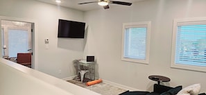 A room with a ceiling fan, a flat-screen TV mounted on the wall, and a window with blinds. - Contemporary two-story home close to the American Museum of Fine Art (Little Rock)