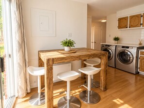A modern kitchen with a wooden table and bar stools, a washing machine, and a potted plant. - Vintage 2 chambres   • Calme • Près métro (Montréal)