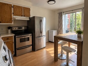 A modern kitchen with stainless steel appliances, wooden cabinets, and a dining area with a table and bar stools. - Vintage 2 chambres • Calme • Près métro (Montréal)