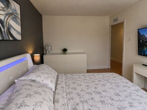 A bedroom with a bed, bedside table, lamp, dresser, and a painting on the wall. - Vintage 2 chambres • Calme • Près métro (Montréal)