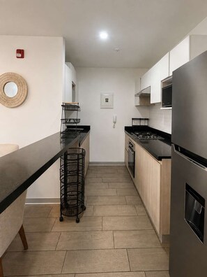 A modern kitchen with a long countertop, a stainless steel refrigerator, and a microwave. - 3 dormitorios Piscina y rooftop P. Libre (Pueblo Libre)