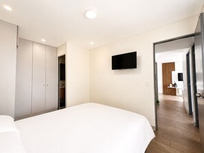 Habitació d'hotel amb llit, armari, televisió i porta que condueix a un bany.