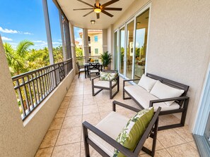 A balcony with a ceiling fan, outdoor furniture, and a view of a residential building. - Luxury Furnished 1-bedroom at Ventana at Tiburon (Naples)