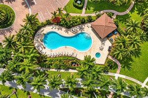 An aerial view of a resort with a large swimming pool, palm trees, and a covered area with lounge chairs. - Luxury Furnished 1-bedroom at Ventana at Tiburon (Naples)