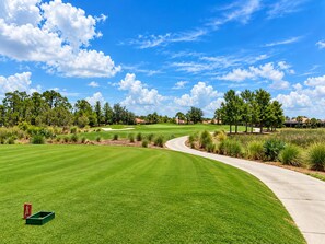A golf course with a well-maintained green, a curved pathway, and a clear blue sky. - Luxury Furnished 1-bedroom at Ventana at Tiburon (Naples)