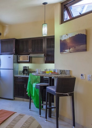 A compact kitchen with dark cabinets, a refrigerator, a microwave, and a dining area with two wicker chairs and a table. - Group Villa. Everyone Gets Their Own Suite. Private Pool. Heart of Sayulita. (Sayulita)