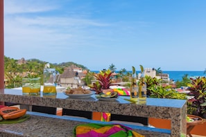 Eine Terrasse mit Blick auf den Ozean, ein Tisch mit Speisen und Getränken sowie eine Flasche Corona Bier.
