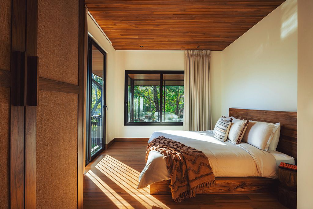 A bedroom with a large bed, a window with curtains, and a view of greenery outside.
