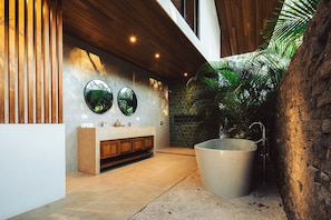 A modern bathroom with a wooden ceiling, a large bathtub, and a stone wall.