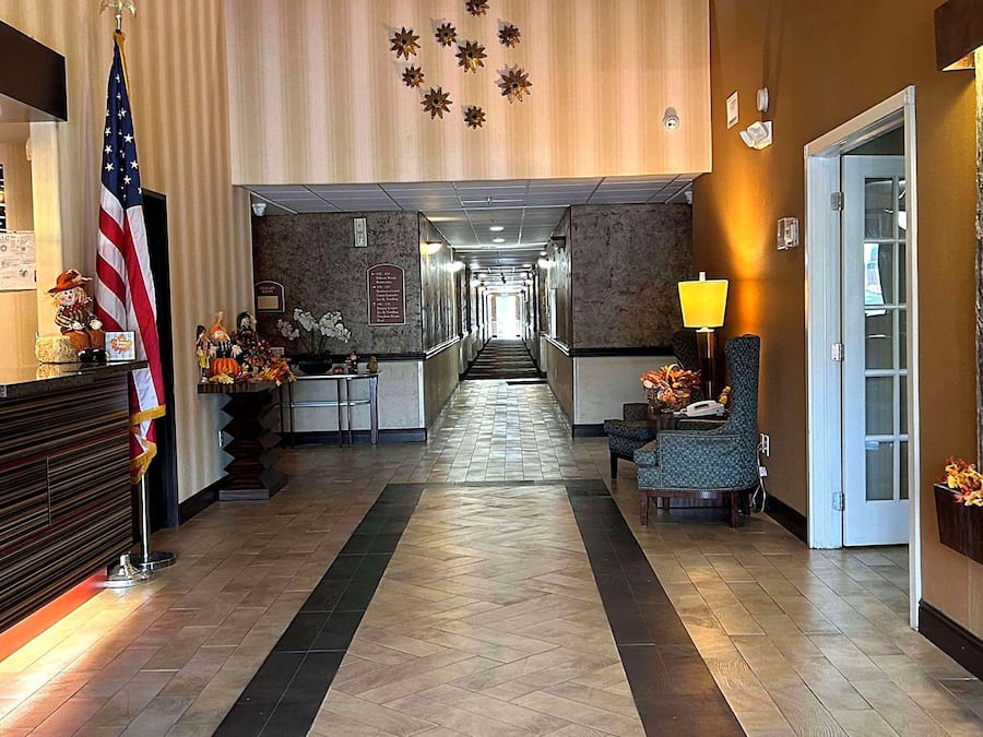 Vestíbulo de hotel con mostrador de recepción, una bandera estadounidense, zona de recepción, pasillo y área de estar con una lámpara.
