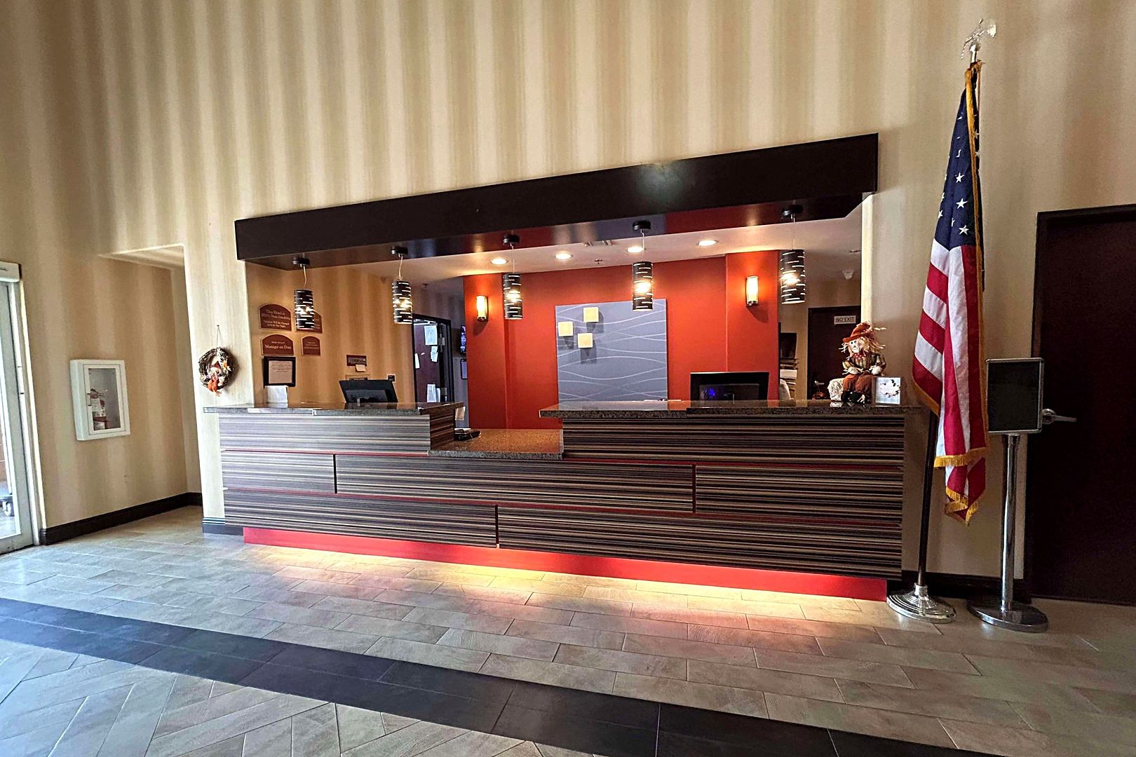 A hotel reception area with a reception desk, a flag, and a wall-mounted information board.