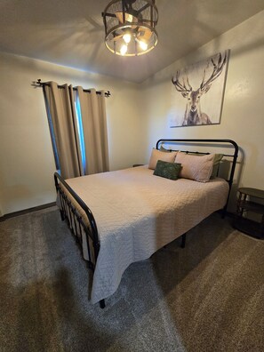 Ein Schlafzimmer mit einem Bett, einem Deckenventilator, einem Fenster mit Vorhängen und einem an der Wand hängenden Gemälde.