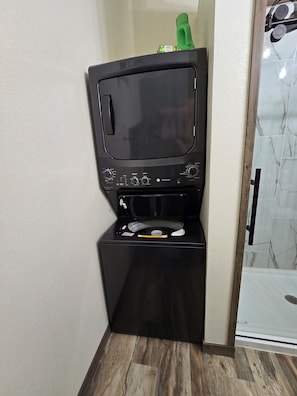 Eine kompakte Waschtrockner-Kombination mit Bedienfeld, platziert in einer Ecke eines Raumes mit Holzboden und gefliestem Spritzschutz.