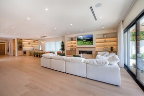 A spacious living area with a large sectional sofa, a flat-screen TV mounted above a fireplace, and a dining area with a wooden table and chairs. - Gaviota Pavilion By Alora Reserve (Los Angeles)