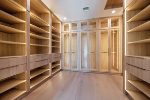 Un armario vestidor con varios estantes y cajones de madera, suelo de madera y un respiradero en el techo.
