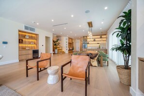 A spacious living area with a dining set, a fireplace, and a kitchen in the background. - Gaviota Pavilion By Alora Reserve (Los Angeles)