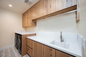 Cocina con armarios de madera, encimera blanca y pileta de acero inoxidable.