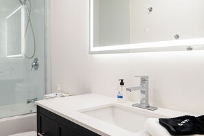 A modern bathroom with a glass shower enclosure, a white sink with a Delta faucet, and a mirror above the sink. - Casa SKKY (Whitehorse)