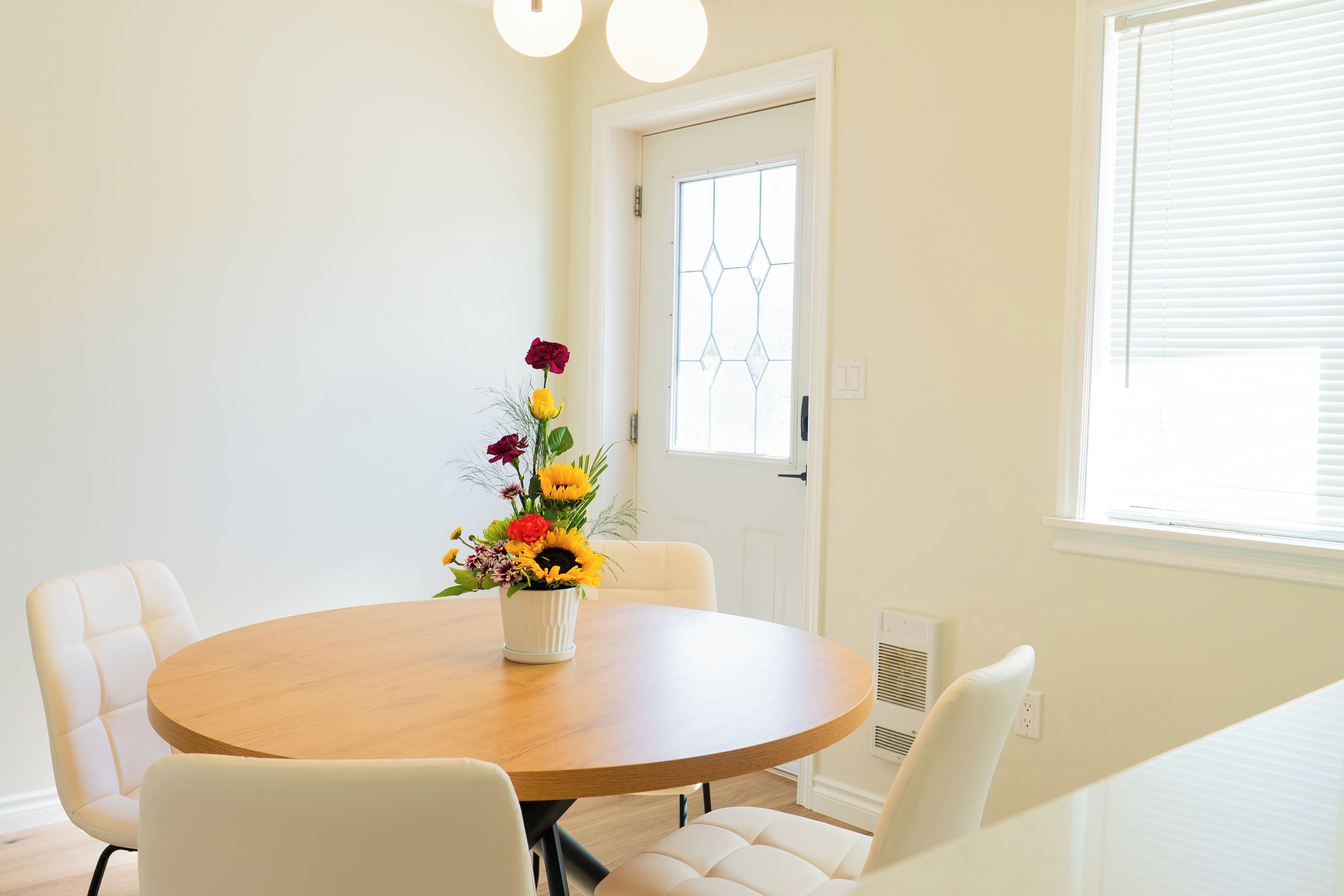 Un coin repas avec une table ronde en bois, des chaises blanches et un arrangement floral.