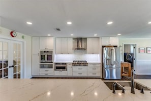 A modern kitchen with white cabinetry, stainless steel appliances, and a marble countertop. - Luxury Farmhouse on 5.6 Acre +Events (Pilot Point)