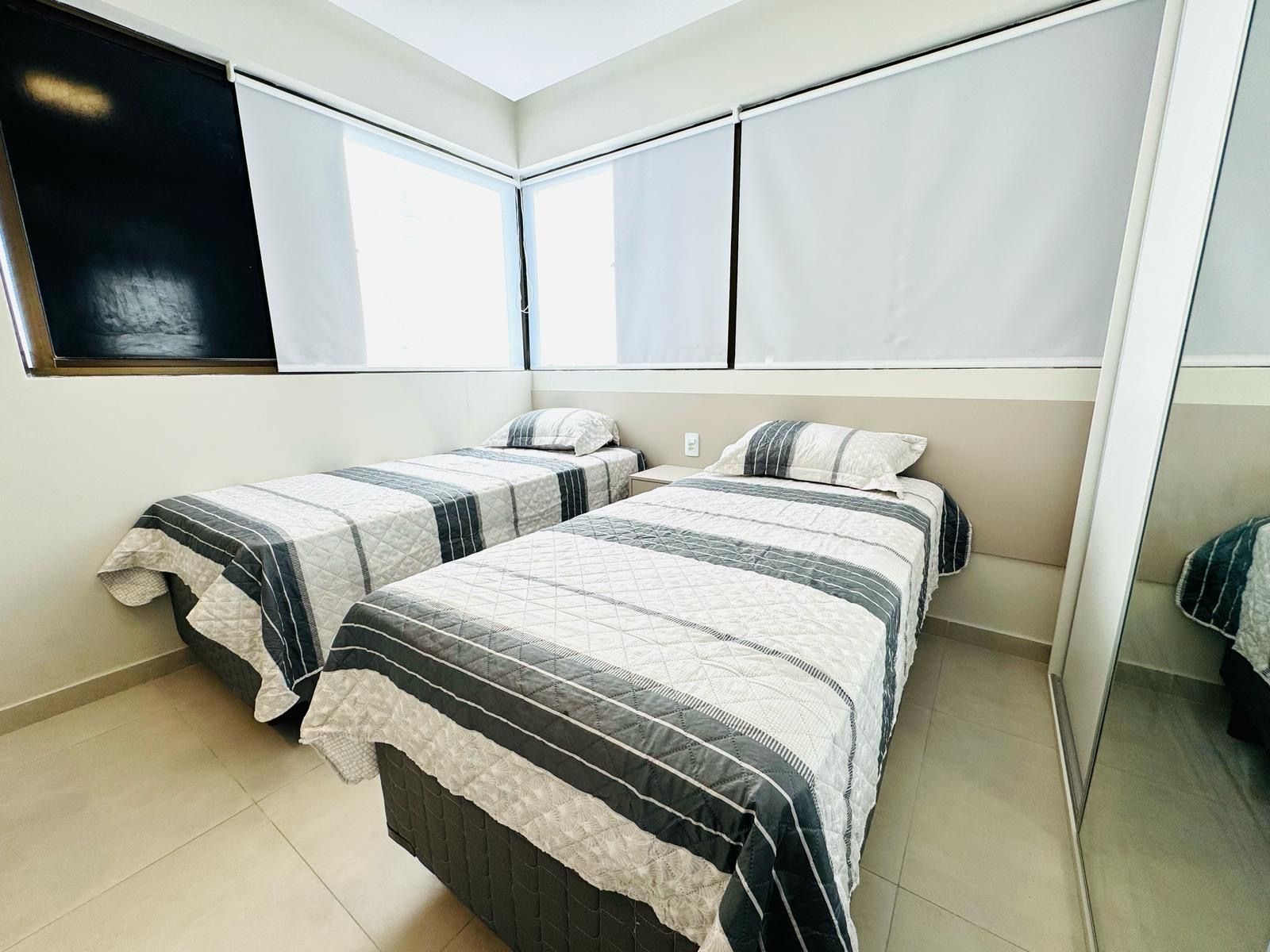 A bedroom with two beds, a large window, and a mirror.
