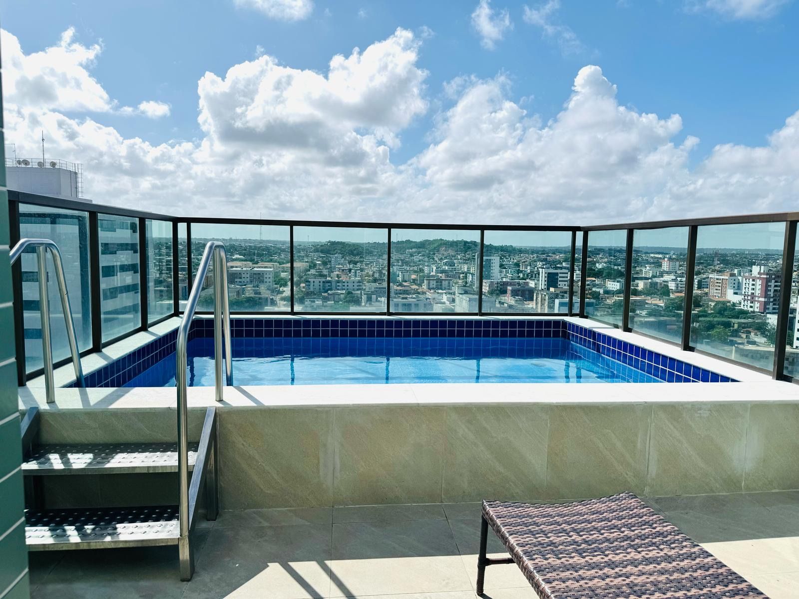 A rooftop swimming pool with a city view, a metal ladder, and a lounge chair.